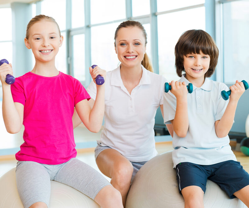 Criança realizando exercícios de musculação com acompanhamento profissional.