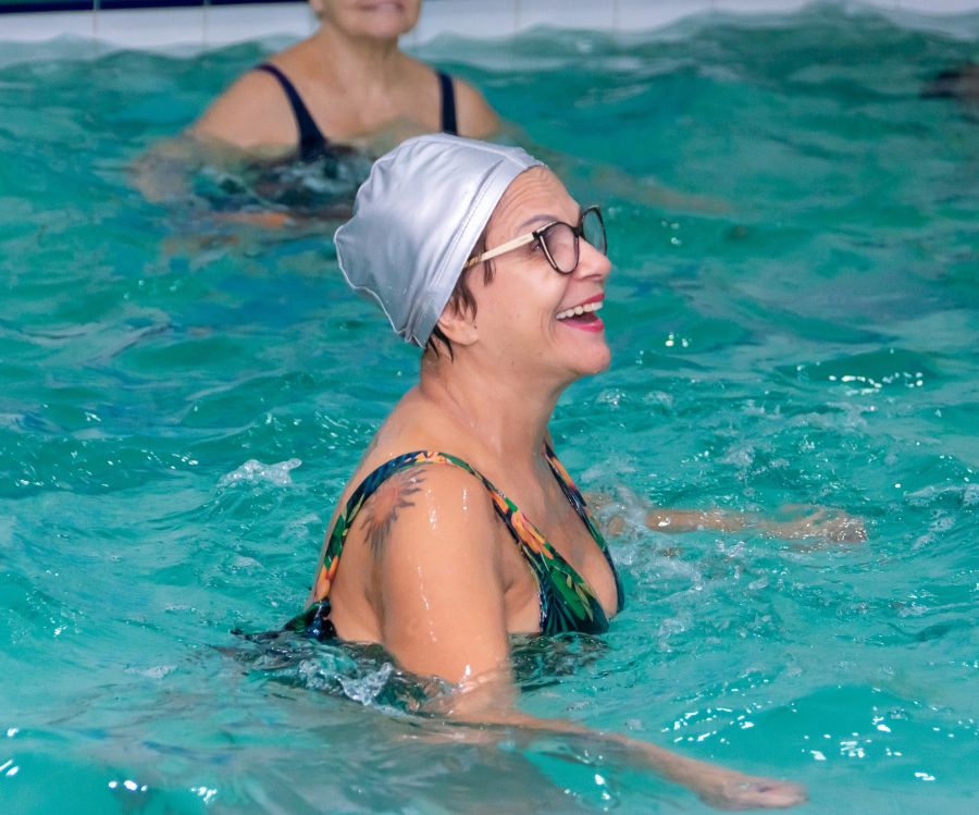 Mulher praticando hidroginástica em piscina aquecida.